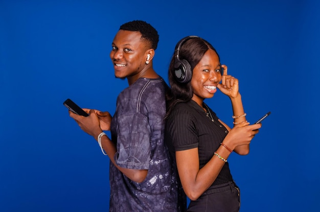 Positive african couple standing back to back holding and using their mobile phones chatting online or scrolling social networks feed