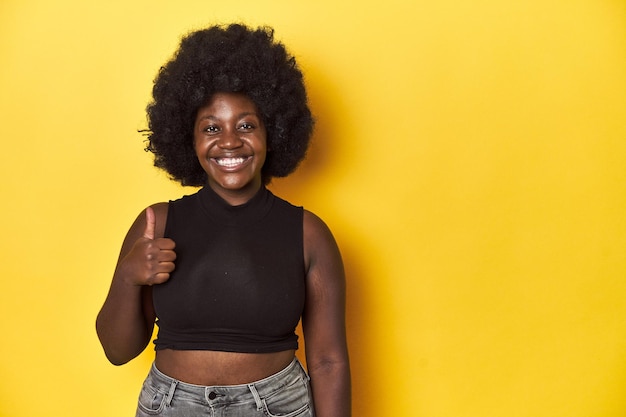 Positive AfricanAmerican woman giving thumbsup on a yellow studio background