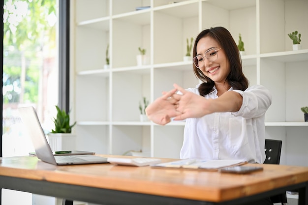 Positive Asian businesswoman stretching her arms and hands at her office desk