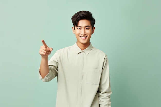 Positive asian man pointing finger aside one color background