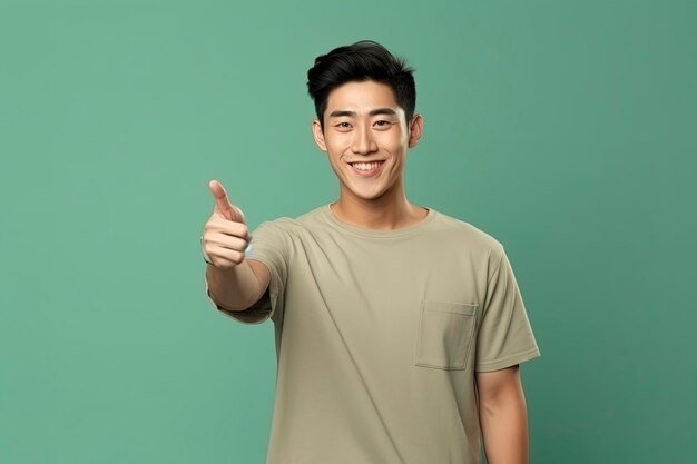 Positive asian man pointing finger aside one color background