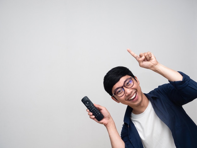 Positive asian man smile holding remote tv and point finger at copy space