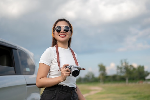 A positive Asian woman in sunglasses travels by car arriving at her destination in the countryside