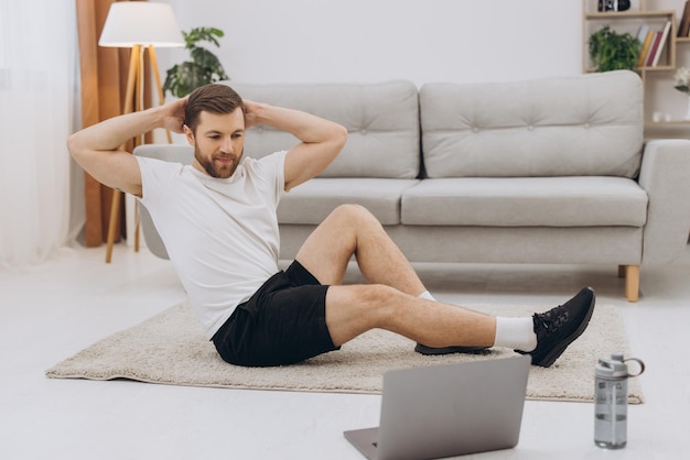 Positive athletic bearded middleaged man stretching at home using laptop watching sport videos on Internet having fitness class online copy space Healthy lifestyle sport on selfisolation