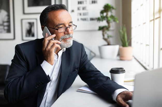 Positive attractive caucasian senior businessman in suit and glasses work calling by smartphone at