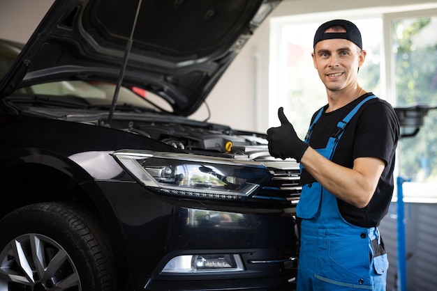 Positive auto service worker smiling to camera and showing thumb up gesture approving car repair