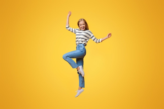 Photo positive beautiful teen girl jumping in air with hands up orange background