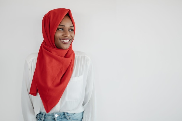 Positive black islamic woman looking aside at copy space over light background and smiling place for text or ad