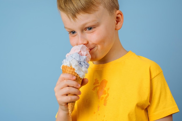 Positive boy licking ice cream on a blue background dirty stain of ice cream on yellow clothes