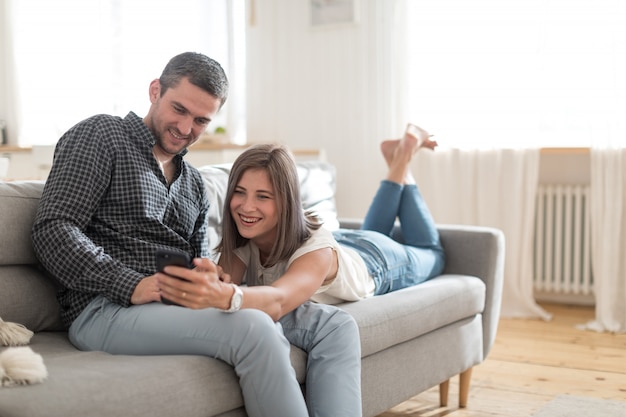 Positive casual couple taking picture on smartphone while resting on couch at home