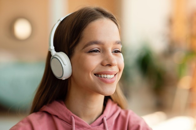 Positive caucasian teenage girl in wireless headphones listening to music and smiling resting at home copy space