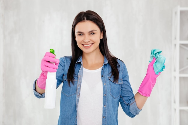 Positive charming female disinfecting the air while holding dust wiper in pink gloved hands