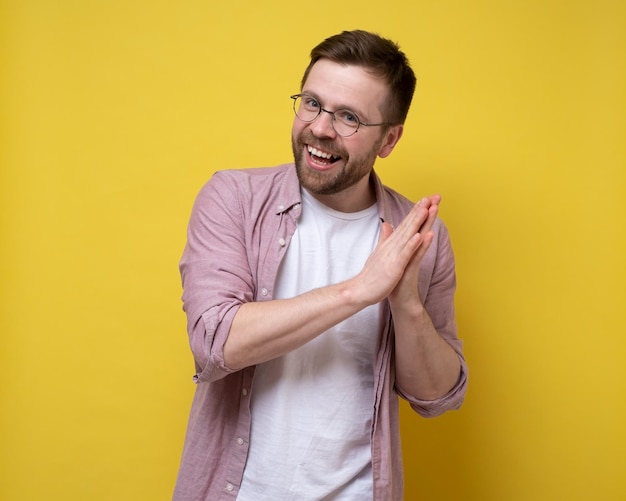 Positive charming man clasped hands together looks at the camera happily and smiling