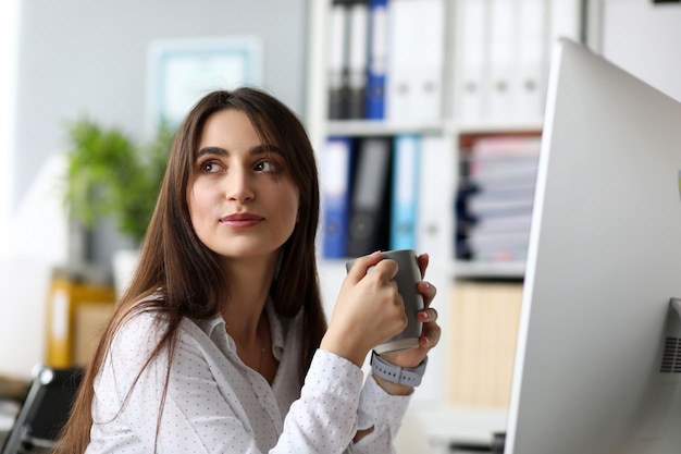 Positive cheerful female sitting at worktable drinking water