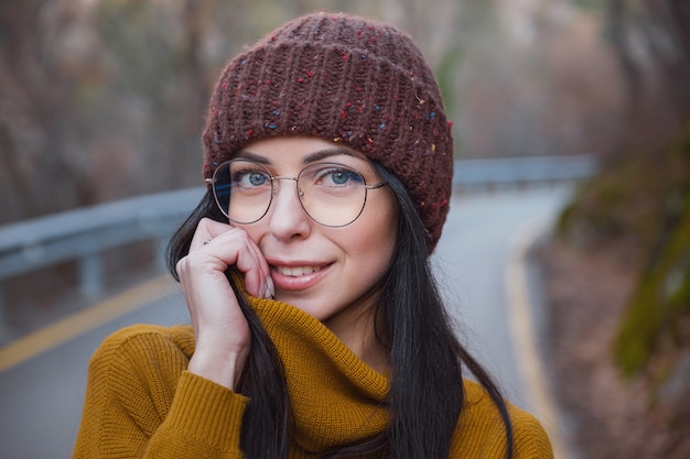 Positive cheerful woman enjoy autumn in park or woods wear yellow pullover and hat, glasses. Mood happy hipster girl in late autumn forest road trip