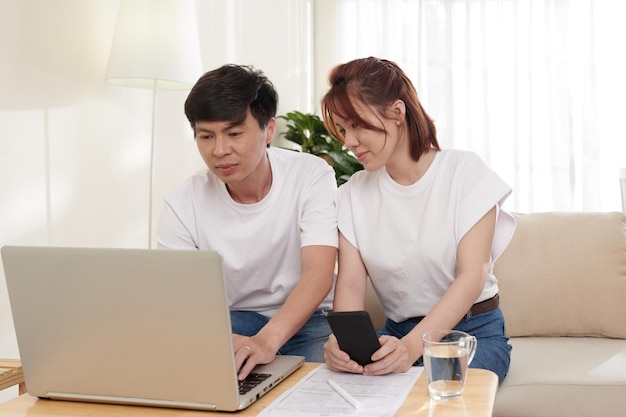 Positive couple managing family finances via form on laptop and filling income tax forms online