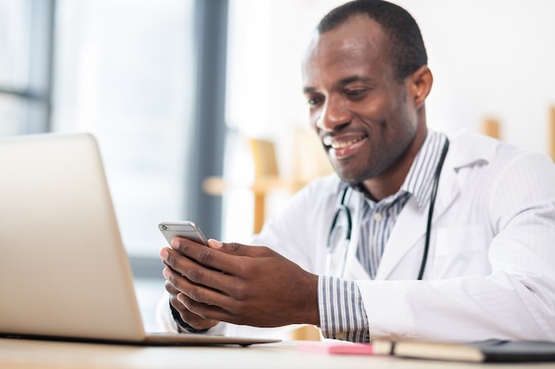 Positive delighted practitioner sitting at his workplace while reading message