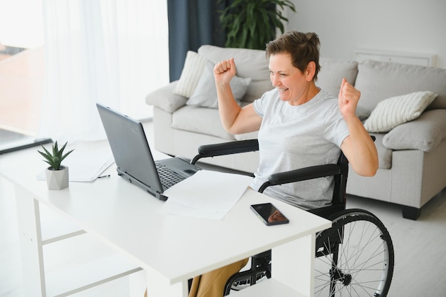 Positive elderly woman in wheelchair working on laptop IT freelancer online