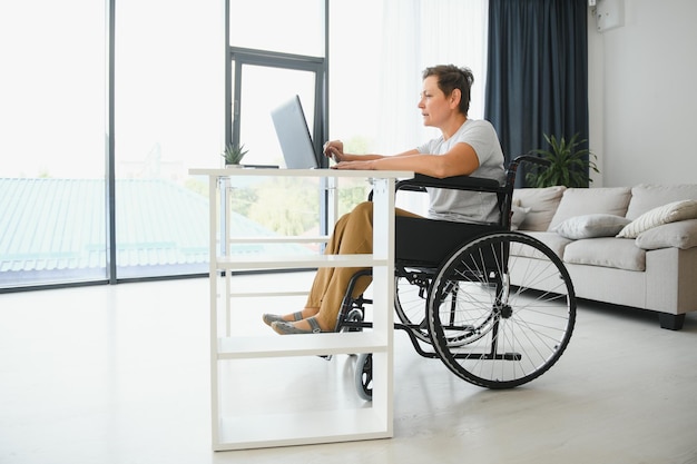 Positive elderly woman in wheelchair working on laptop IT freelancer online