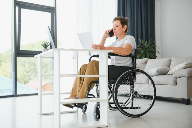 Positive elderly woman in wheelchair working on laptop IT freelancer online