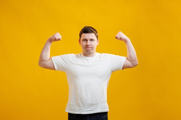 Positive emotional man smiles shows muscles on his arms feels proud to be strong and have strength says I am hero Muscular male athlete raises arms with joy shows how strong he is