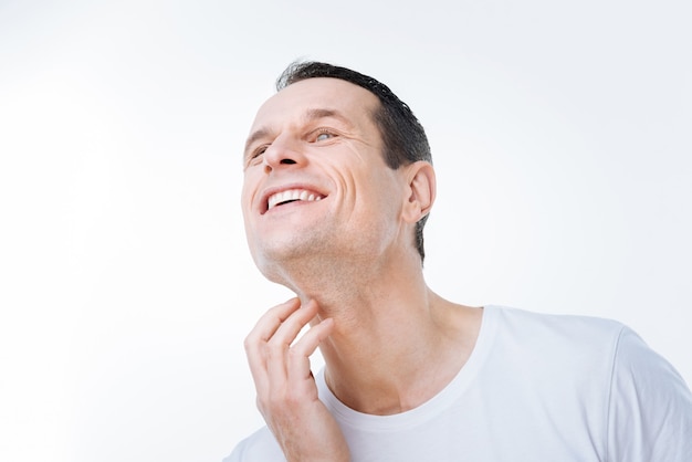 Positive emotions. Nice delighted good looking man touching his neck and smiling while being in a positive mood