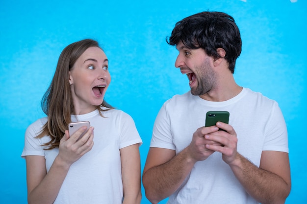 Positive excited man and woman screaming and looking at each other while both using mobile phones