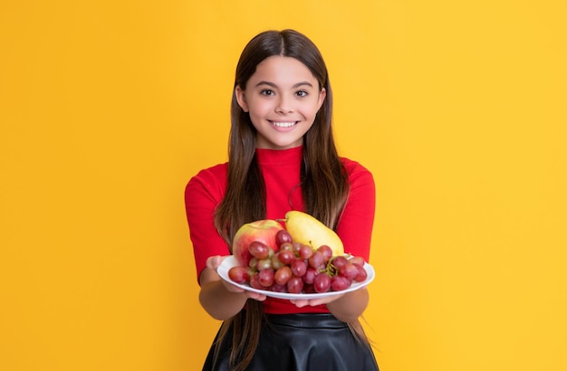 Positive girl hold fresh fruit plate on yellow background selective focus