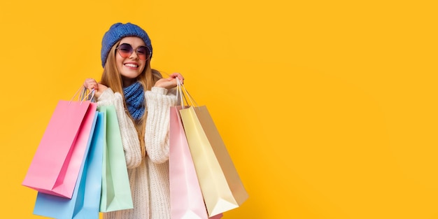 Positive girl in knitted hat and sunglasses holding shopping bags