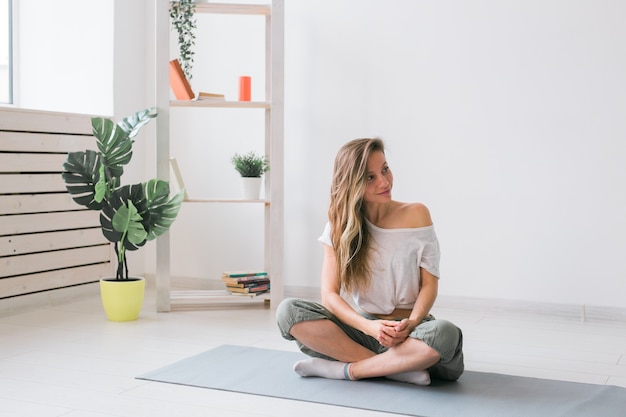 Positive girl sitting on fitness mat resting after pilates or yoga practice. Mindfulness and wellbeing concept.