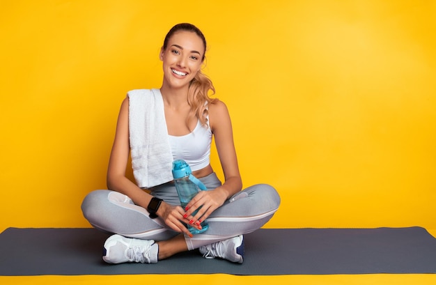 Positive Girl Sitting On Fitness Mat Resting Over Pink Background