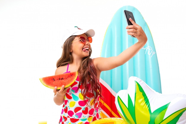 Positive girl in a swimsuit holds a watermelon, is photographed on the phone