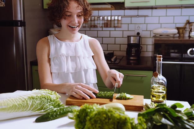 positive girl teenager with brown curly hair, in home kitchen makes vegetarian salad