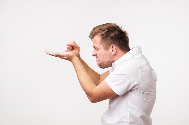 Positive handsome man shows something very tiny or small being in doubtful mood