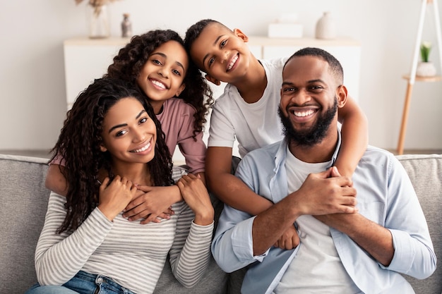 Positive Healthy Relationships Between Parents And Children. Portrait of smiling African American daughter and son hugging mum and daddy from behind. Family of four people of color posing for photo