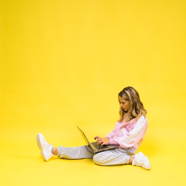 Positive kid sit with laptop read homework wear casual style cloth isolated over yellow background