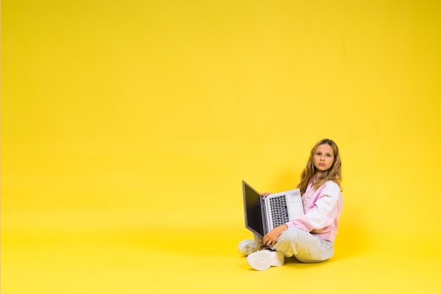 Positive kid sit with laptop read homework wear casual style cloth isolated over yellow background