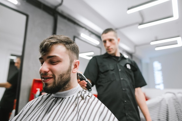 Positive man makes a haircut in a barbershop Professional barber cuts a cheerful client