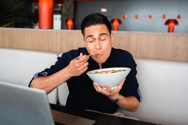 Positive man sitting at table eating a salad chewing