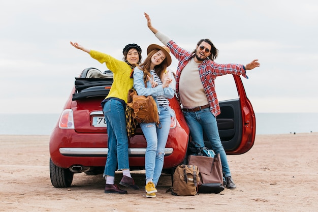 Positive man with upped hands near embracing women and car on sea beach