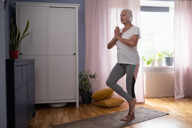 Positive mature lady standing in tree pose keeping balanced exercising