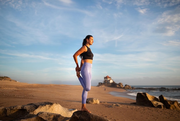 Positive millennial caucasian woman practice yoga enjoy breathing exercises leg stretching on sea