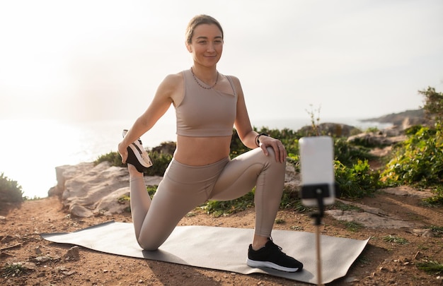 Positive millennial caucasian woman in sportswear doing leg stretching exercise shoots video on