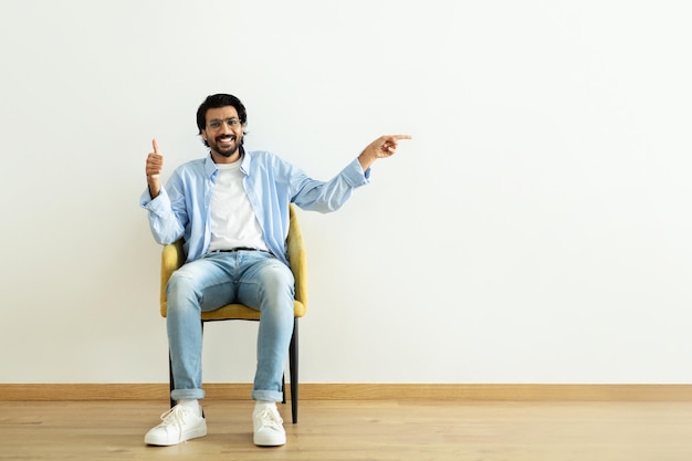 Positive millennial middle eastern guy show thumb up approving pointing finger at empty space