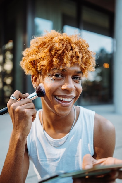 Photo positive multiracial charismatic boy preparing makeup at his face with visage brush while standing a