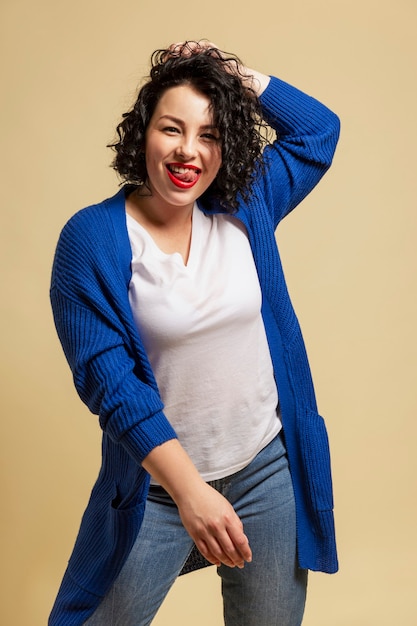 Positive plump girl. Young beautiful brunette in a blue sweater and jeans laughs. Yellow background. Vertical.