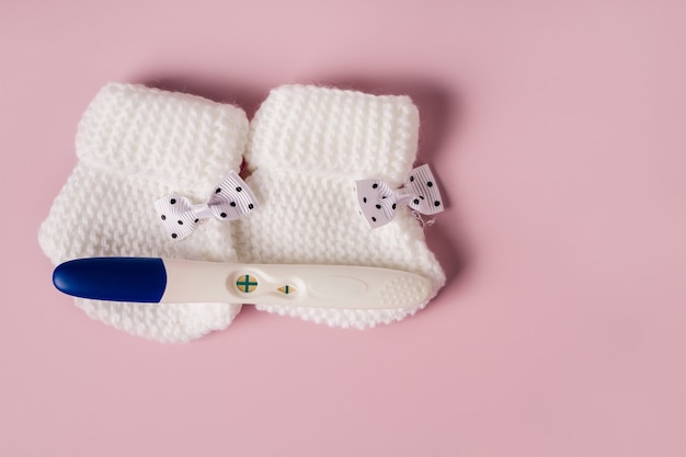 A positive pregnancy test and baby booties on a pink background Waiting for the baby