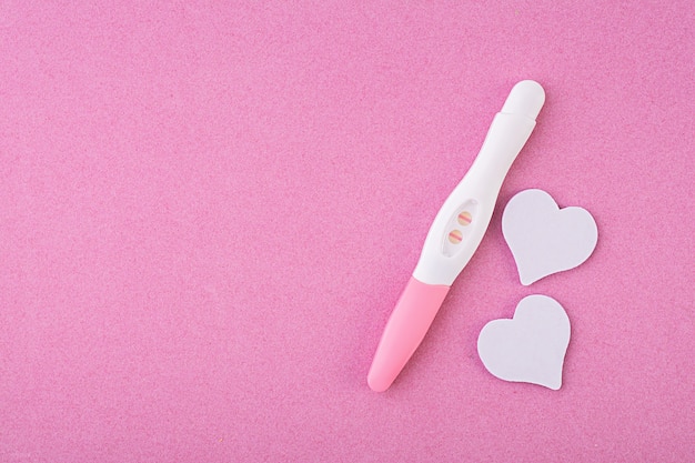 Positive pregnancy test with hearts isolated on pink background