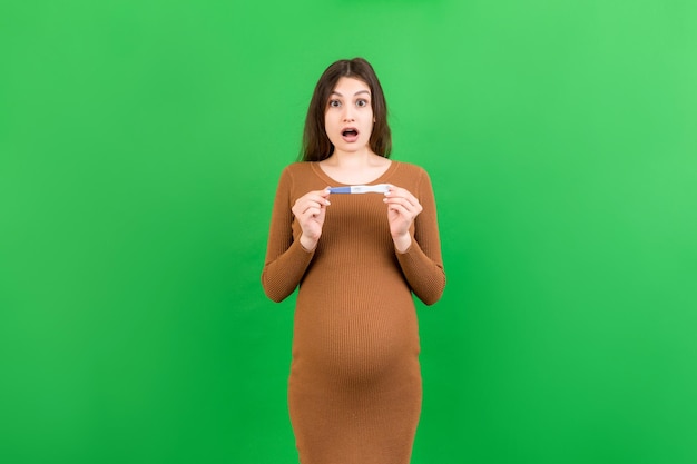 Positive pregnancy test with two stripes against happy pregnant woman abdomen at Colored background Future mother in gray dress Pregnancy surprise Copy space