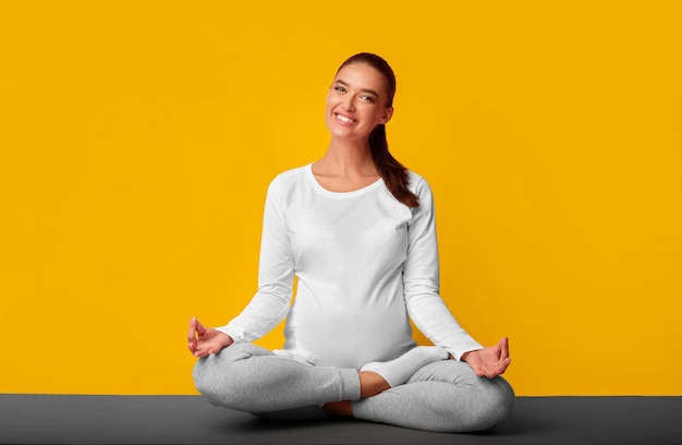 Photo positive pregnant woman meditating sitting in lotus pose in studio